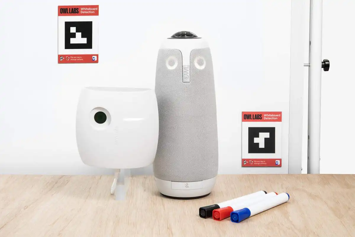 Whiteboard Owl 1080p Collaboration Camera – Image 5 Whiteboard Owl video conferencing device with whiteboard detection feature, alongside a whiteboard marker holder and markers on a wooden table, against a minimalist background.